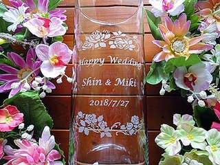 「Happy wedding」「新郎と新婦の名前」「結婚式の日付」「バラの花の飾り」を、側面に彫刻した円柱形のガラス花器(結婚祝いの贈り物)
