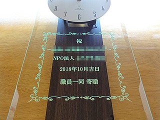 「祝 NPO法人○○、日付、職員一同」を彫刻した、NPO法人の周年祝い用の掛け時計