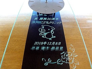「祝開院20周年、クリニックの名前とイメージキャラクター」を彫刻した、周年祝い用の掛け時計