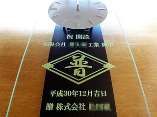 「会社のマーク」と「祝 開設、有限会社○○御中」を彫刻した、営業所の開設祝い用の掛け時計