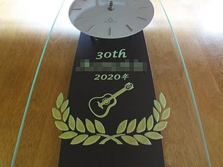 「30th、ペンションの名前、日付、ギターのイラスト」を前面ガラスに彫刻した、ペンションの30周年祝い用の掛け時計