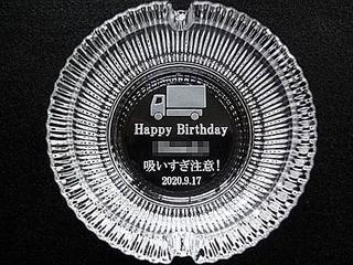 「Happy Birthday 吸いすぎ注意、贈る相手の名前、誕生日の日付、トラックのイラスト」をガラス製灰皿の底面に彫刻した、誕生日プレゼント用の灰皿