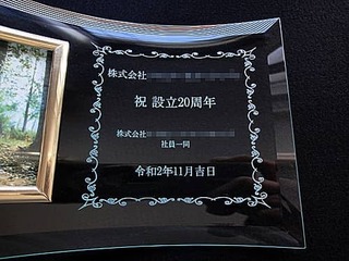 「株式会社○○ 祝設立20周年 株式会社○○社員一同」を彫刻した、周年祝い用のガラス製写真立て