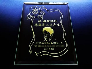 「先生の似顔絵」と「祝教授就任 ○○先生 ○○一同」を彫刻した、教授就任祝いの贈り物用のガラス盾