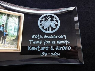 「家紋、50th anniversary、Thank you as always、両親の名前、日付」を彫刻した、両親の金婚式祝い用のガラス製写真立て