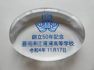 「校章、創立50年記念 ○○高等学校、創立記念日の日付」を彫刻した、創立50周年の記念品用のガラス製ペーパーウェイト