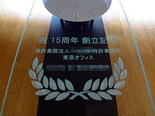 「祝 15周年 創立記念 特許業務法人○○特許事務所、贈り主の会社名」を前面ガラスに彫刻した、特許事務所の周年祝い用の掛け時計