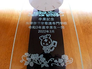 「卒業記念 ○○看護専門学校 令和3年度卒業生一同」と「マスコットキャラクター」を前面ガラスに彫刻した、卒業生から学校へ寄贈する振り子時計