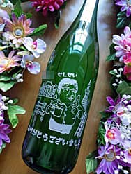 卒業生から研究室の教授へ贈るお酒(先生の似顔絵入りのイラスト、先生の名前、感謝を込めたメッセージを、日本酒の一升瓶の側面に彫刻)