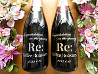 「Congratulations on the opening、開業日の日付」と「カフェのロゴ」をボトル側面に彫刻した、カフェの開業祝い用のシャンパン