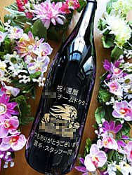 祝還暦、贈る相手の名前、スポーツチームのロゴマーク、贈り主の名前を一升瓶の側面に彫刻した、チームドクターの還暦祝い用の日本酒