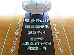 「祝教授就任 ○○先生、○○大学○○研究室同窓生一同より」を前面ガラスに彫刻した、教授就任祝い用の掛け時計