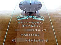 「クリニックの名前、日付、○○大学卒業生有志一同」を彫刻した、開院祝い用の掛け時計