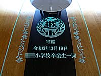 卒業生から小学校へ寄贈する掛け時計(校章と、寄贈 令和3年3月 ○○小学校卒業生一同を、掛け時計の前面ガラスに彫刻)