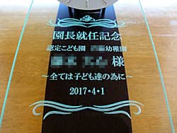 「園長就任記念 ○○様」「幼稚園の名前とスローガン」を前面ガラスに彫刻した、幼稚園の園長就任祝い用の掛け時計