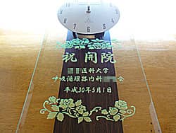 「祝開院、○○医科大学○○科より」を前面ガラスに彫刻した、開院祝い用の掛け時計