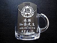 卒業生から担任の先生へ贈るマグカップ(校章と、感謝 ○○先生 卒業生一同を、ガラス製マグカップの側面に彫刻)