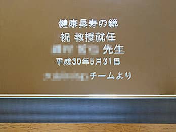 「お祝いメッセージ、贈る相手の名前、就任日の日付、贈り主の名前」を表面に彫刻した、教授就任祝い用の鏡