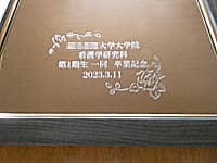 「○○大学大学院 看護学研究科 第一期生一同卒業記念」を表面に彫刻した、卒業生から大学へ寄贈する鏡