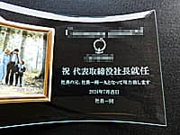 会社のロゴマーク、祝 代表取締役社長就任、就任日の日付、贈り主の名前を彫刻した、社長就任祝い用のガラス製写真立て