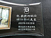 「校章、祝教授御就任 ○○先生、就任日の日付、贈り主の名前」を彫刻した、教授就任祝い用の名入れ写真立て