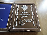 園長就任祝い用の写真立て(園長先生の似顔絵と保育園のマーク、祝園長就任 ○○先生 ○○保育園職員一同を、ブックタイプの写真立てに彫刻)