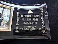 教授就任祝い用の写真立て(大学のマークと、教授御就任記念 ○○先生 ○○医科大学○○科大学院生一同を、ガラス製の写真立てに彫刻)