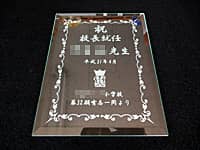 「祝 校長就任 ○○先生、校章、○○一同より」を彫刻した、校長就任祝い用のガラス盾