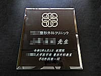 「クリニックのマーク」と「○○整形外科クリニック ○○先生 祝開院 ○○大学医学部整形外科教室一同」を彫刻した、クリニックの開院祝い用のガラス盾