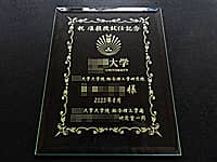 「大学のシンボルロゴ、祝准教授就任記念 ○○様、就任日の日付、贈り主の名前」を彫刻した、准教授就任祝い用のガラス盾