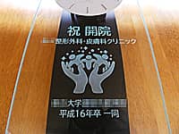 「祝開院、クリニックの名前とマーク、贈り主の名前」を前面ガラスに彫刻した、クリニックの開院祝い用の壁掛け時計
