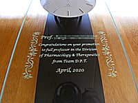 新教授の名前、お祝いメッセージ、贈り主の名前、就任日の日付を前面ガラスに彫刻した、教授就任祝い用の壁掛け時計